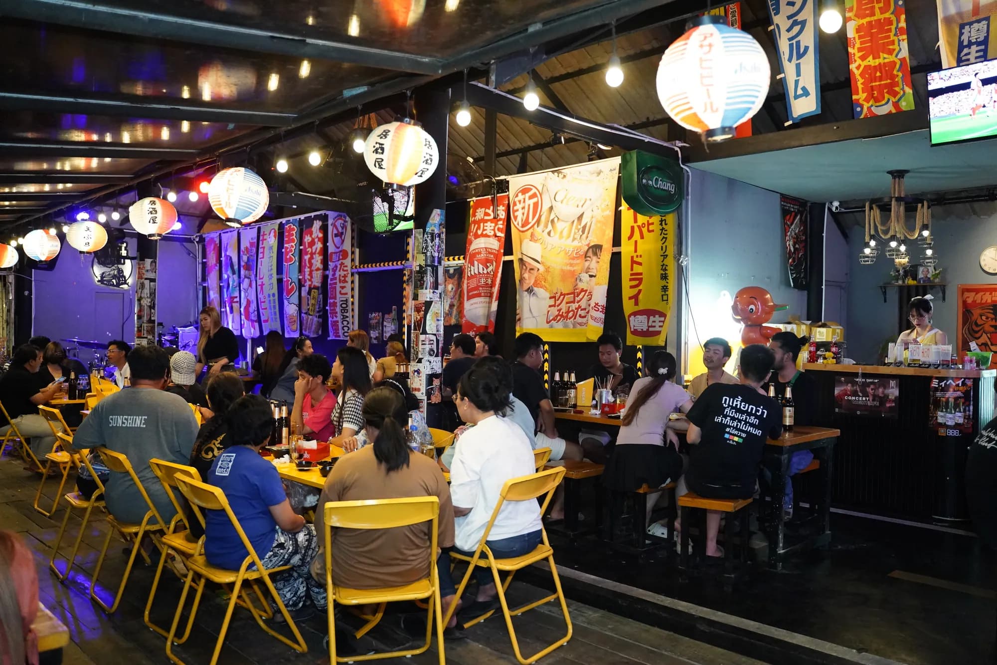 คืนคึกคักคนเต็มร้านใต้โคมไฟญี่ปุ่นและป้าย izakaya ที่ Mara Station — แก๊งเพื่อนหลังเลิกงาน
