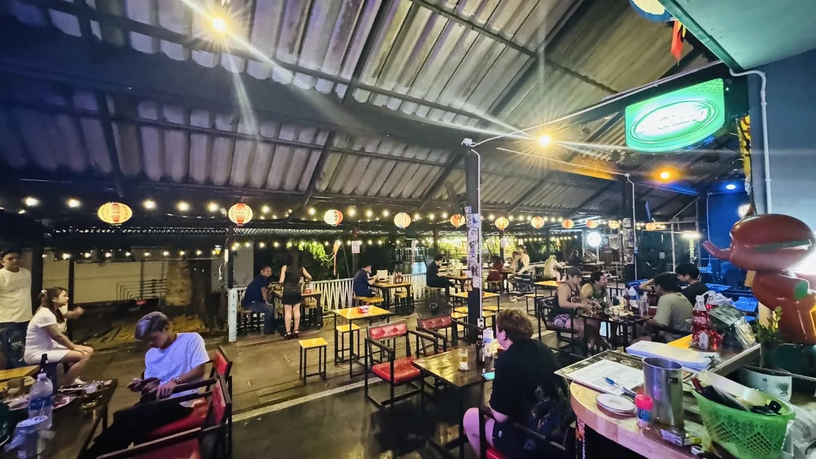 มุมกว้างร้าน Mara Station ยามค่ำ — โต๊ะไม้ โคมไฟ และลูกค้านั่งกินดื่ม