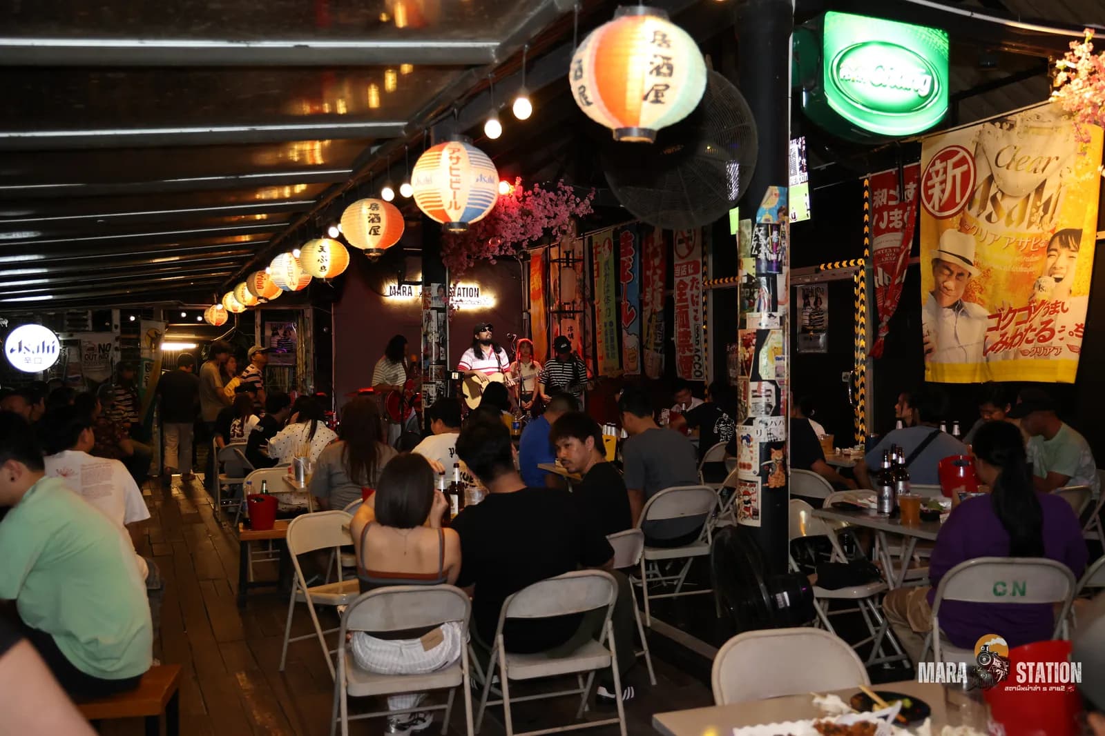 บรรยากาศคืนวงสดที่ Mara Station — โต๊ะลูกค้าเต็มร้านใต้โคมไฟญี่ปุ่น