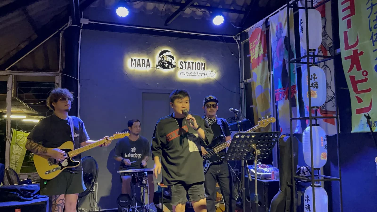 วงดนตรีสดเต็มวงบนเวที Mara Station ใต้ป้ายนีออน